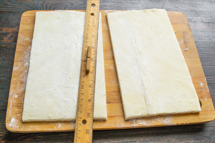 How to Cut Puff Pastry Evenly A sheet of puff pastry being cut in half on a floured surface.