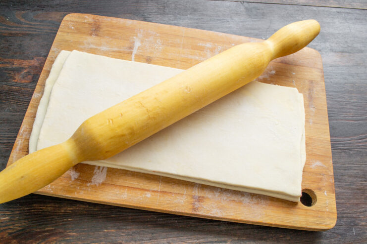 Rolling Out the Puff Pastry Dough A rolling pin rolling out a sheet of puff pastry on a floured board.