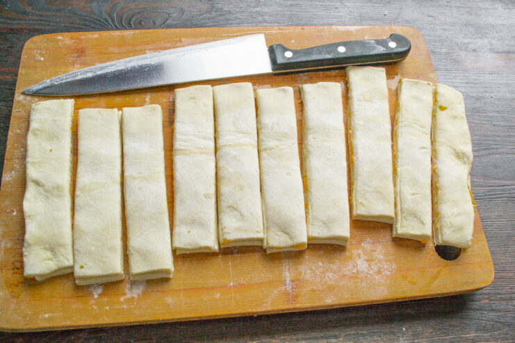 Slicing the Pastry into Strips for Cheese Sticks A knife cutting the layered puff pastry into even strips.