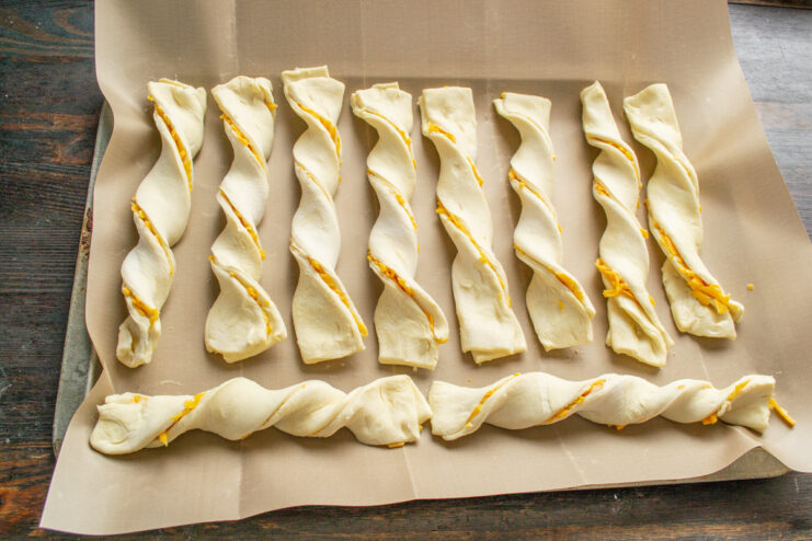 Creating the Perfect Twist for Cheese Sticks A hand twisting a strip of cheese-filled puff pastry into a spiral shape.