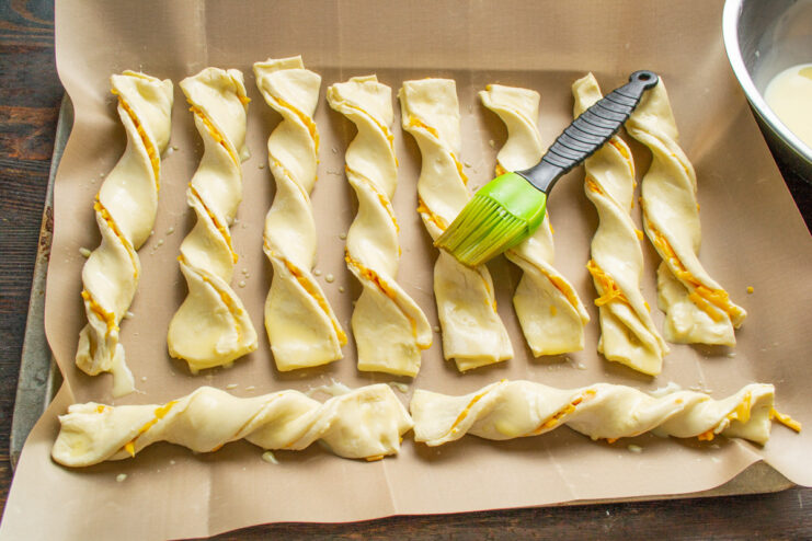 Brushing with Egg Wash for a Golden Finish A pastry brush applying egg wash to twisted cheese sticks on a baking sheet.