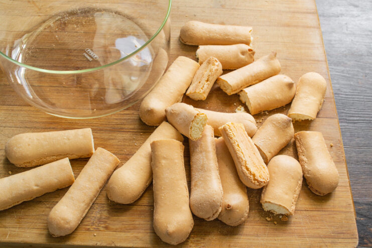 Trimming savoiardi biscuits (ladyfingers) with a knife to fit the height of a glass dessert dish.