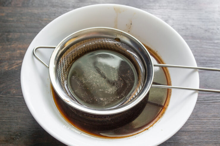 Pouring amaretto liqueur from a bottle into a bowl of cooled coffee.