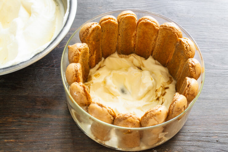 Arranging coffee-dipped ladyfingers vertically around the inside of a glass dish.
