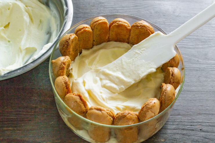 Spreading a thick layer of mascarpone cream over the savoiardi biscuits in the dish.