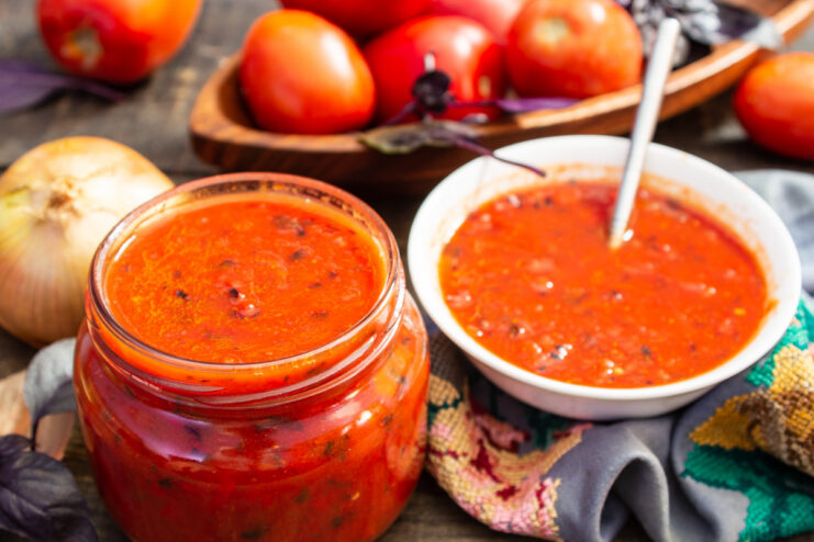 A glass jar filled with vibrant red tomato sauce with basil and vegetable chunks, ready to be served.