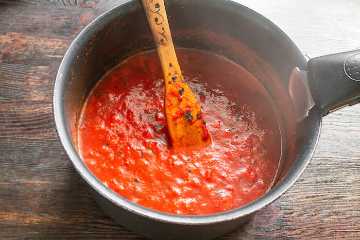Seasoning the Tomato Sauce to Perfection A spoon tasting the finished tomato sauce from a saucepan to adjust seasoning.