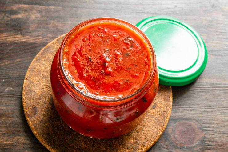 Storing the Homemade Tomato Sauce for Later Use Hot tomato and basil sauce being poured into a clean, dry glass jar for storage.