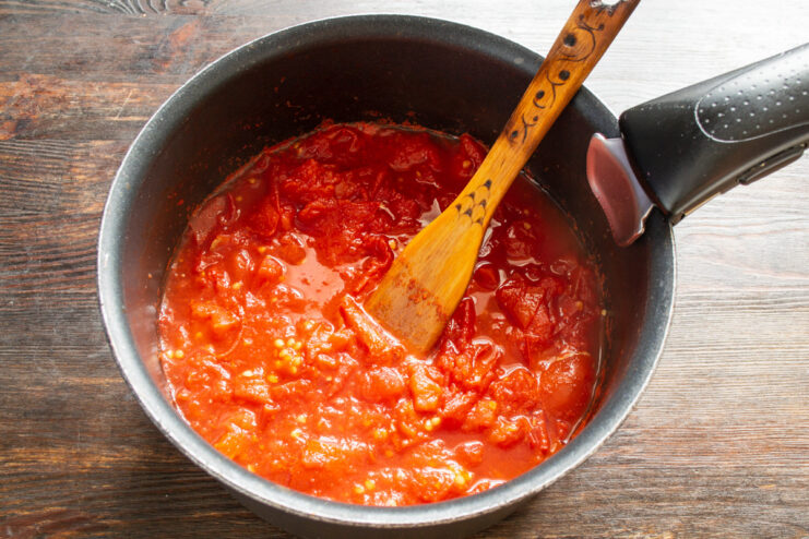 Simmering Tomatoes Until Soft and Pulpy Tomatoes simmering in a saucepan on the stove, breaking down into a thick soup.
