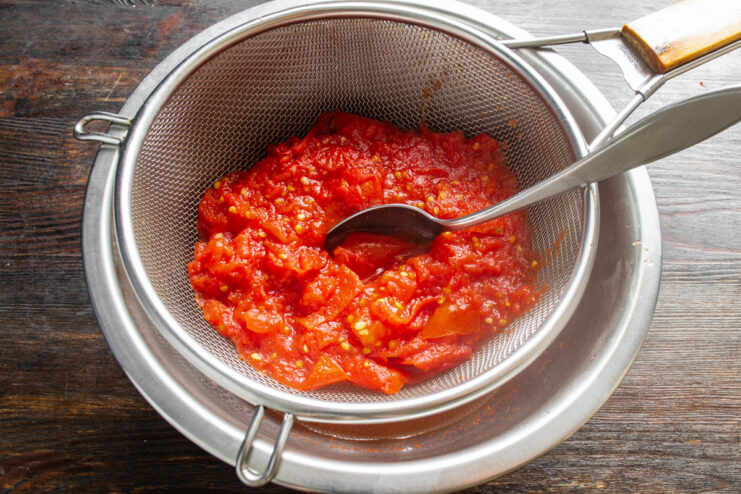 Straining the Cooked Tomatoes for a Smooth Base Cooked tomatoes being poured from a saucepan into a fine sieve set over a bowl.