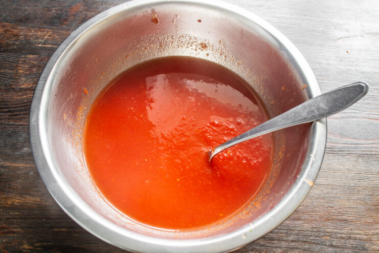 Creating a Silky Smooth Tomato Purée A hand using a spoon to press cooked tomatoes through a sieve to separate skins and seeds.