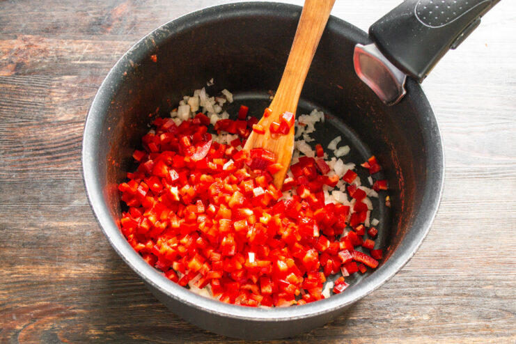 Incorporating Sweet Bell Peppers for Extra Flavor Finely diced red bell pepper being added to a saucepan with diced onions.