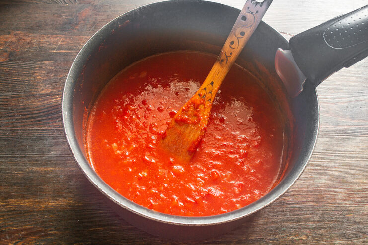 Reducing the Sauce to Concentrate Flavors Tomato sauce with vegetables simmering vigorously in a saucepan to thicken.