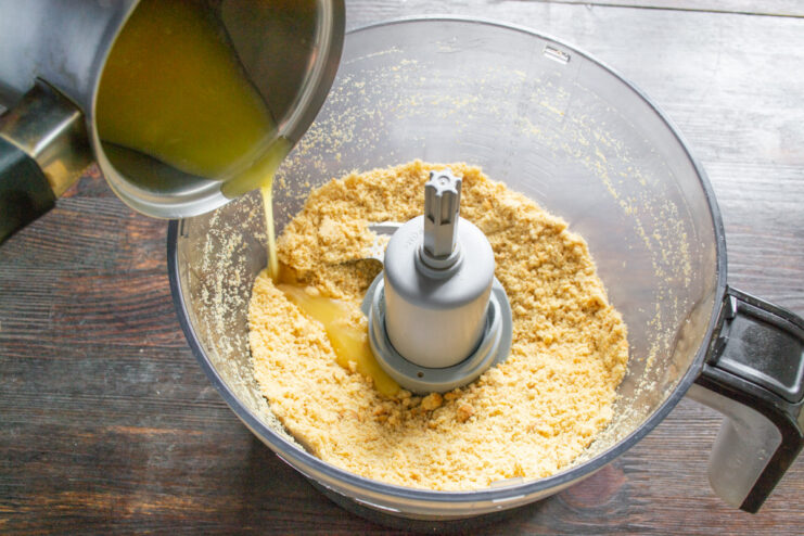 Step 2: Combining the Crust Ingredients Melted butter and milk being poured over a bowl of fine cookie crumbs.