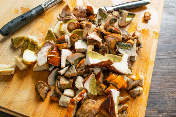 Close-up of fresh wild mushrooms being chopped into large pieces on a cutting board.