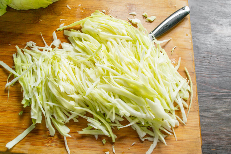 Thinly shredded white cabbage in a bowl, sprinkled with salt.