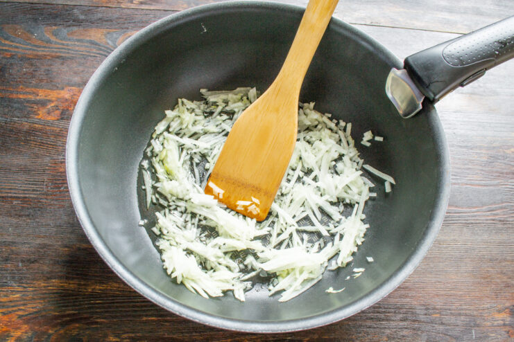 Chopped onions being sautéed in a hot skillet with oil.