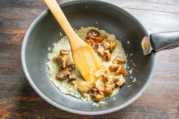 Cooked wild mushrooms and onions being fried together in a skillet.