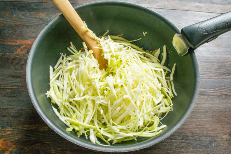 Shredded cabbage and mushrooms braising in a covered skillet on low heat.