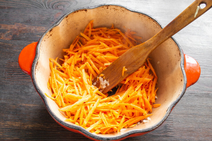 Adding Grated Carrots to the Onion and Garlic Mixture Grated carrots being added to the pan with sautéed onions and garlic.
