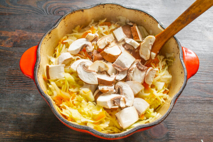 Adding Coarsely Chopped Mushrooms to the Pot Coarsely chopped cremini mushrooms being added to the pot with cabbage and other vegetables.