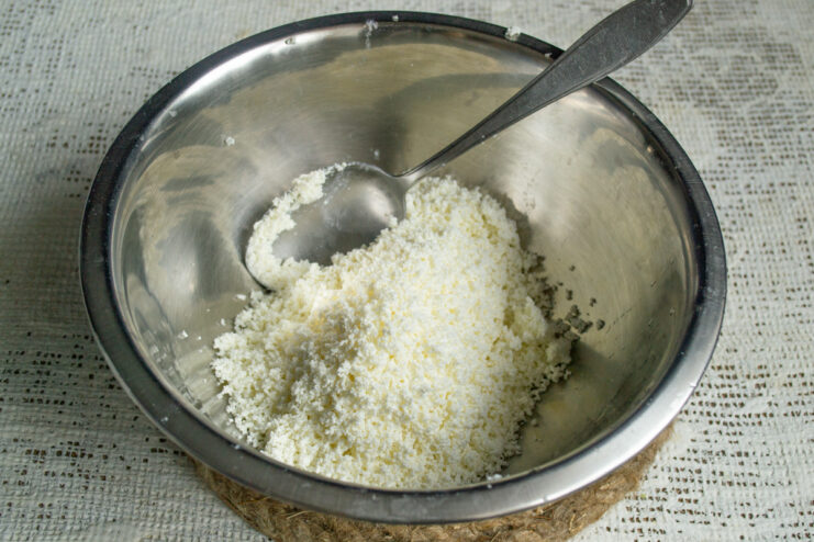 Sifting Tvorog for a Smooth Cake Batter A bowl of tvorog (farmer's cheese) being pressed through a fine-mesh sieve with a spoon.