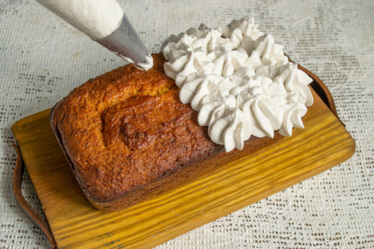 Decorating the Cooled Loaf Cake with Whipped Cream Piping whipped cream from a piping bag with a star tip onto the cooled pumpkin loaf cake.