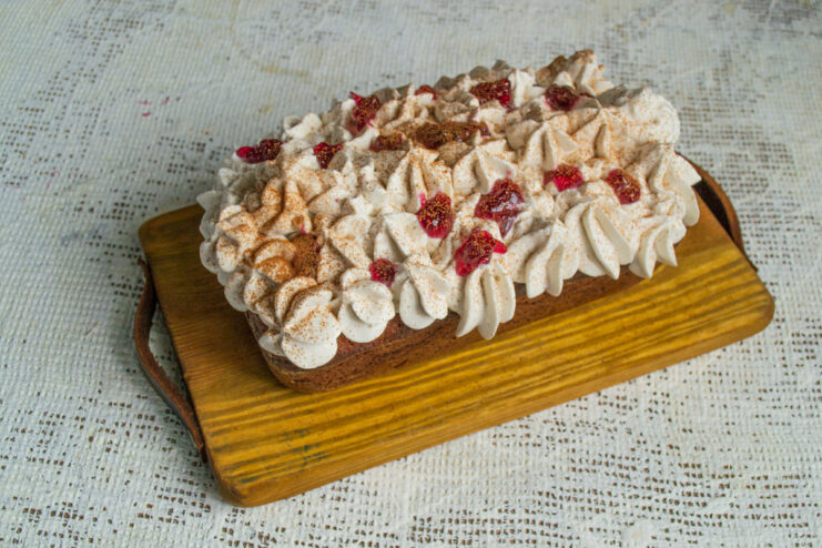 Final Touches: Jam and Spices for Decoration The finished tvorog and pumpkin loaf cake decorated with whipped cream, fruit jam, and a sprinkle of cinnamon.