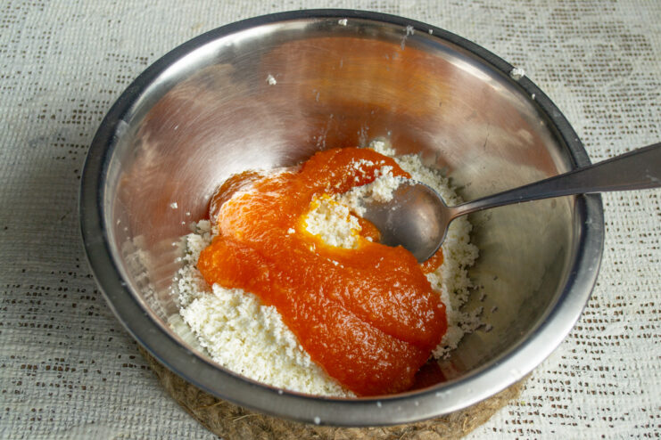 Combining Pumpkin Puree with Tvorog A bowl with sifted tvorog and a spoonful of orange pumpkin puree being added to it.