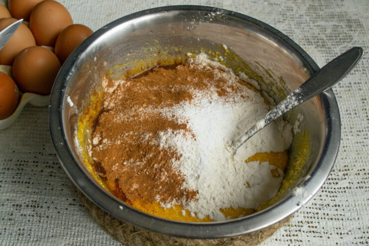 Adding Warm Spices to the Cake Batter A teaspoon of ground cinnamon being added to the flour in the mixing bowl.