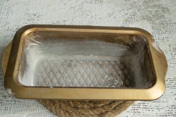 Preparing the Loaf Pan for Baking A rectangular metal loaf pan being greased and floured in preparation for baking.