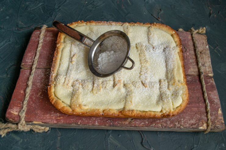 The final touch: Dusting the freshly baked pie with powdered sugar. Dusting the golden-brown baked Tvorog pie with powdered sugar using a small sieve.