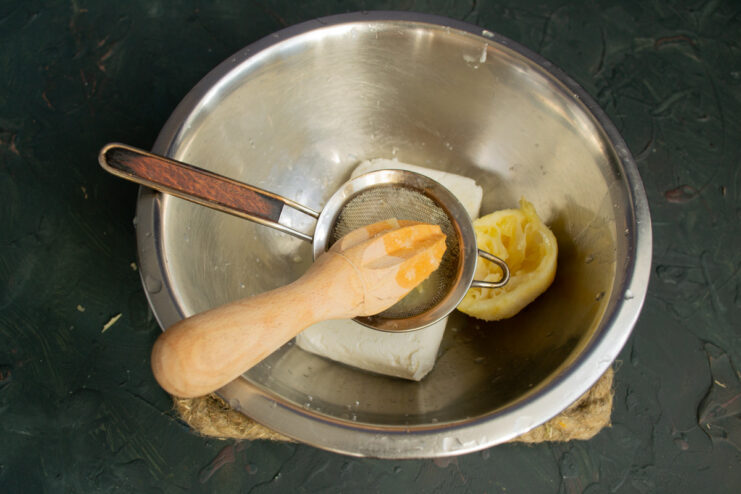 Making the filling: Combining fresh lemon juice with dry cottage cheese. A bowl of dry tvorog (cottage cheese) with freshly squeezed lemon juice being added.