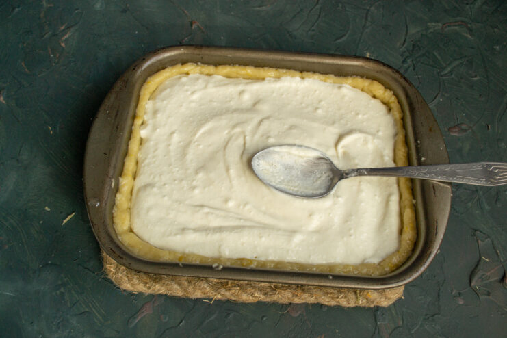 Assembling the pie: Spreading the creamy cottage cheese filling over the crust. Pouring the smooth cottage cheese filling into the dough-lined rectangular baking dish.