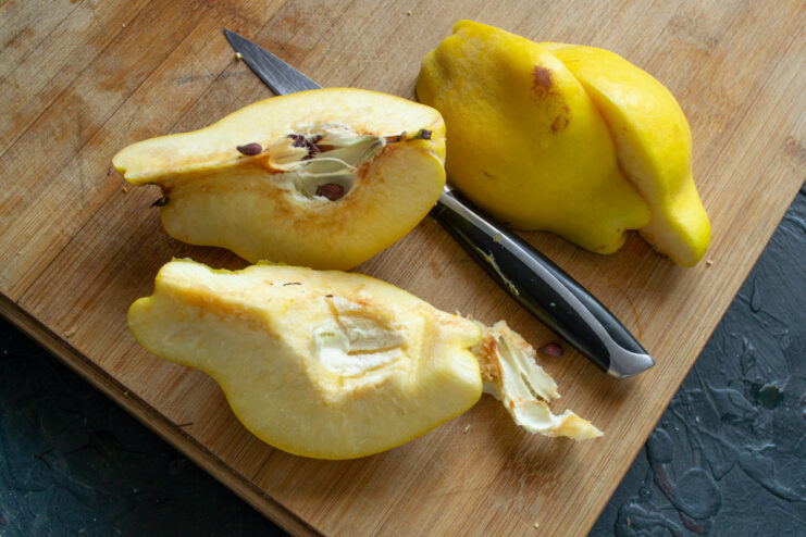 Preparing the Quince: Quartering and Coring the Fruit for Jam Quince cut into quarters on a wooden board, with the core and seeds being removed.