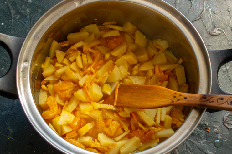 Simmering the Fruit: Cooking Quince and Mandarins Until Soft A covered pot on the stove, with the fruit mixture inside coming to a boil.