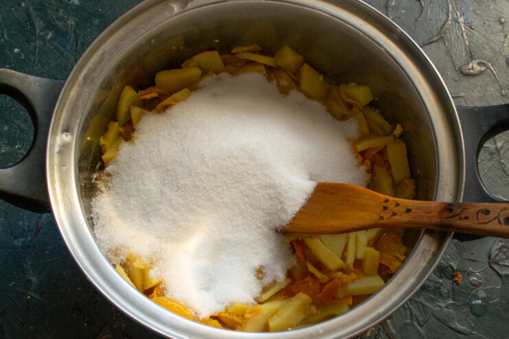 Sweetening the Jam: Adding Sugar to the Softened Fruit Granulated sugar being poured into the pot with the softened quince and mandarin mixture.