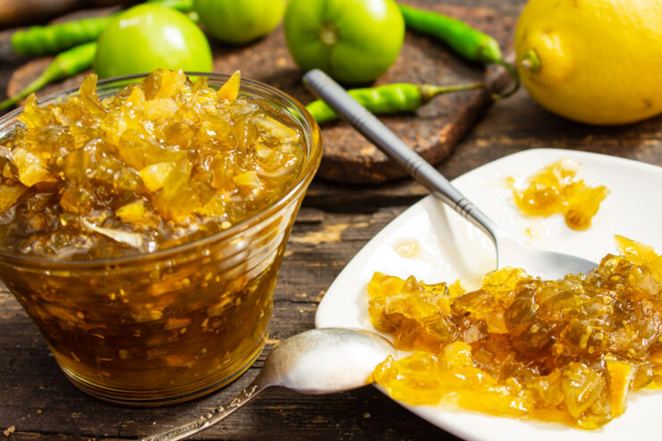 A glass jar of homemade green tomato jam with a spoon, ready to be served.