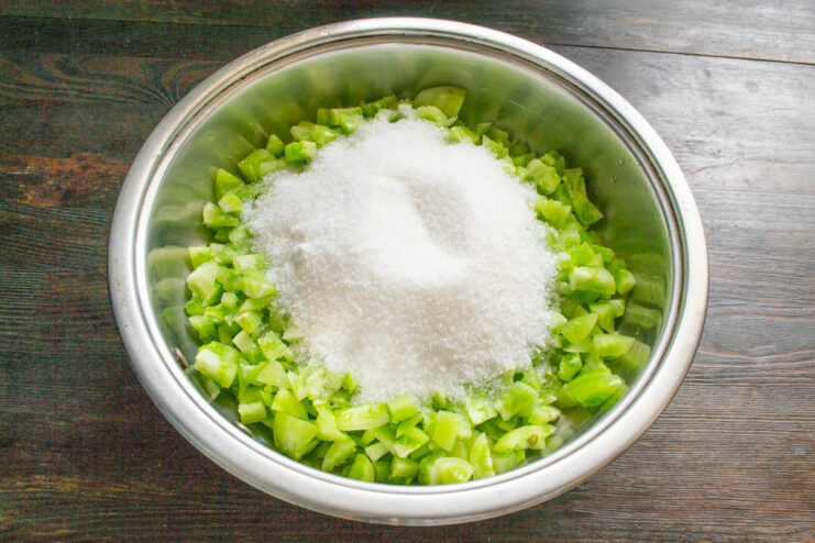Adding Sugar to the Green Tomatoes Granulated sugar being poured over chopped green tomatoes in a pan.