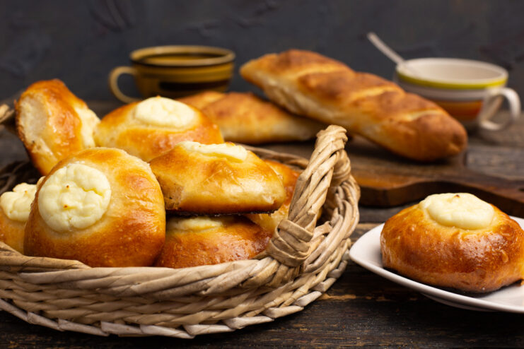 A wooden board with freshly baked golden Vatrushki sweet cheese buns and a crusty baguette.