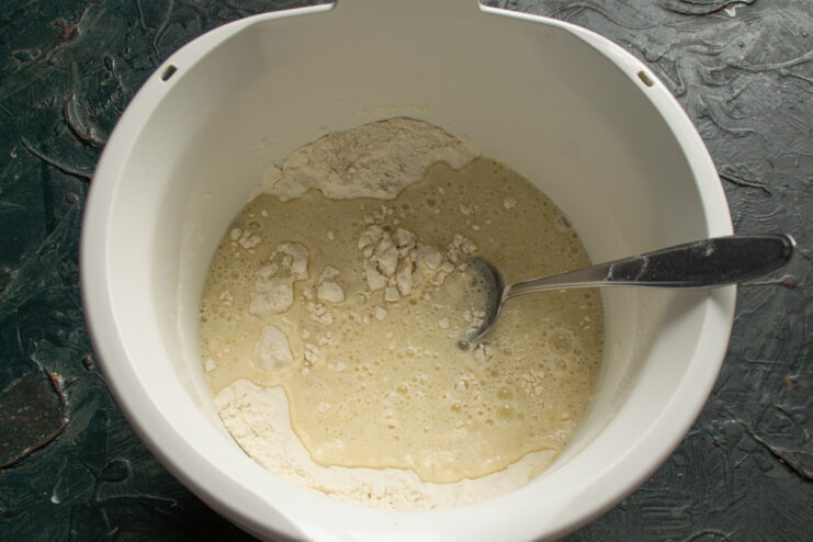Combining Wet and Dry Ingredients for Vatrushki Pouring the warm milk mixture into the bowl with flour and yeast.