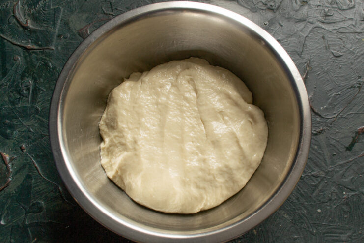 Placing the Dough in a Greased Bowl to Rise A ball of smooth dough being placed into a large, lightly oiled glass bowl.