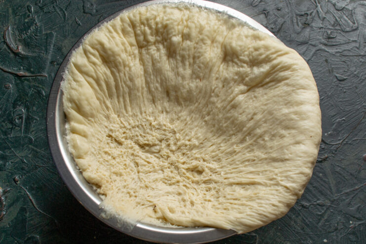 Punching Down the Risen Dough A hand punching down the fluffy, risen yeast dough in a glass bowl.