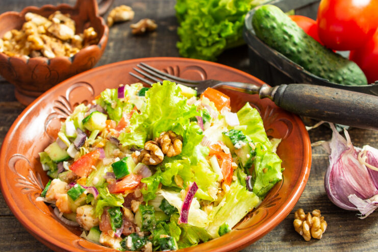 A serving of vegan salad with walnuts, tofu, tomatoes, and lettuce in a white bowl.