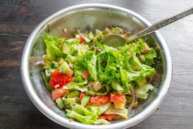Gently tossing the salad to combine all ingredients with the dressing. Tossing the vegan salad with two spoons to evenly coat all ingredients with dressing.