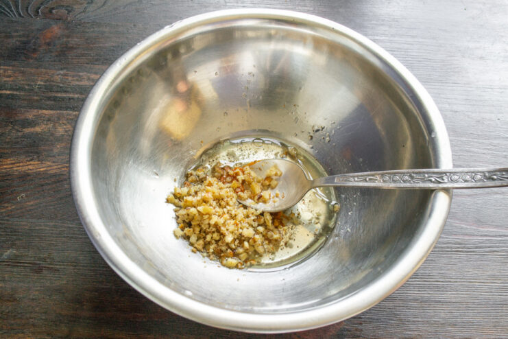 Adding crushed walnuts to the dressing for a crunchy texture. Crushed walnuts being stirred into the olive oil and lemon juice dressing in a bowl.