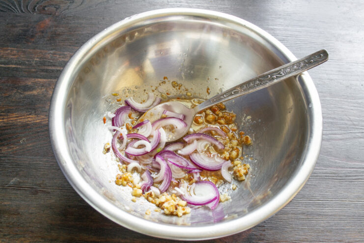 Slicing red onion thinly for the vegan salad. A red onion being sliced into thin half-rings on a cutting board.