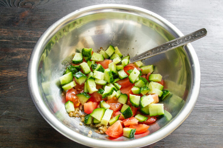 Chopping fresh cucumbers to add to the salad. Fresh cucumbers being diced into cubes on a cutting board.