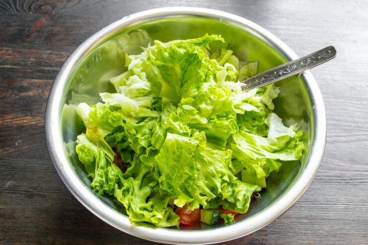 Adding fresh, crisp lettuce to the salad bowl. Coarsely chopped lettuce being added to a bowl with other salad ingredients.