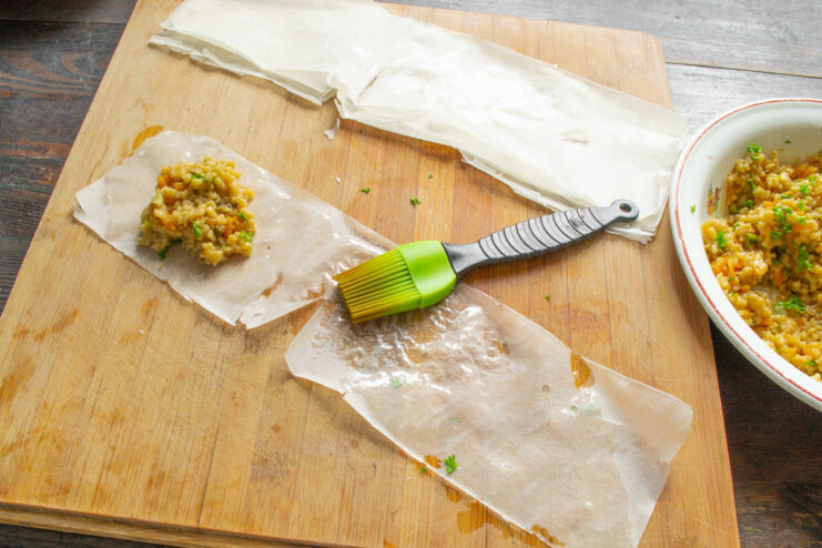 Filling the Phyllo Dough for Samsa Two tablespoons of bulgur and vegetable filling placed on the edge of a phyllo dough strip.